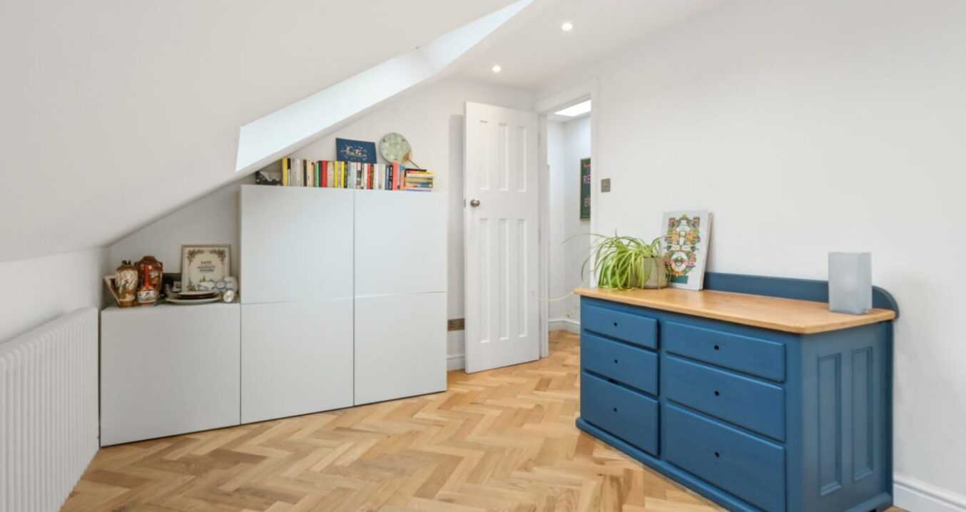 Loft conversion room with timber flooring, sloping ceiling, low storage and blue cabinet for an Epping CM16 property.