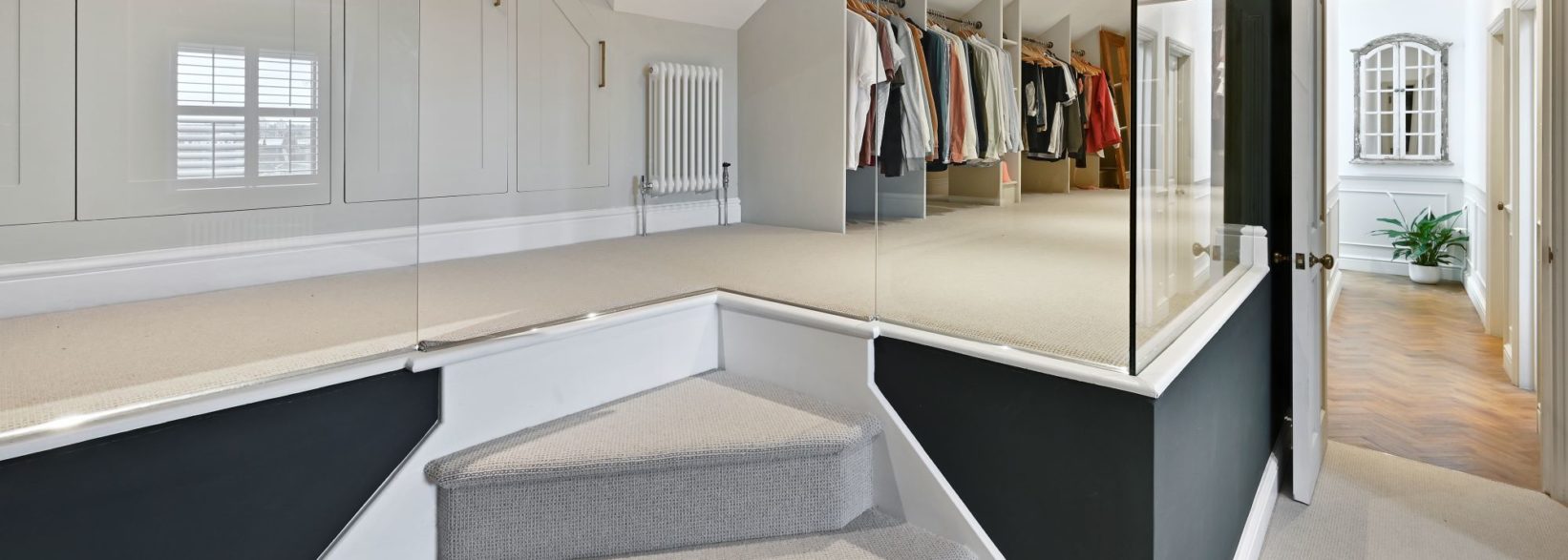 Loft dressing area with fitted wardrobes, carpeted floor and hallway access, supporting Palmers Green N13 loft design.