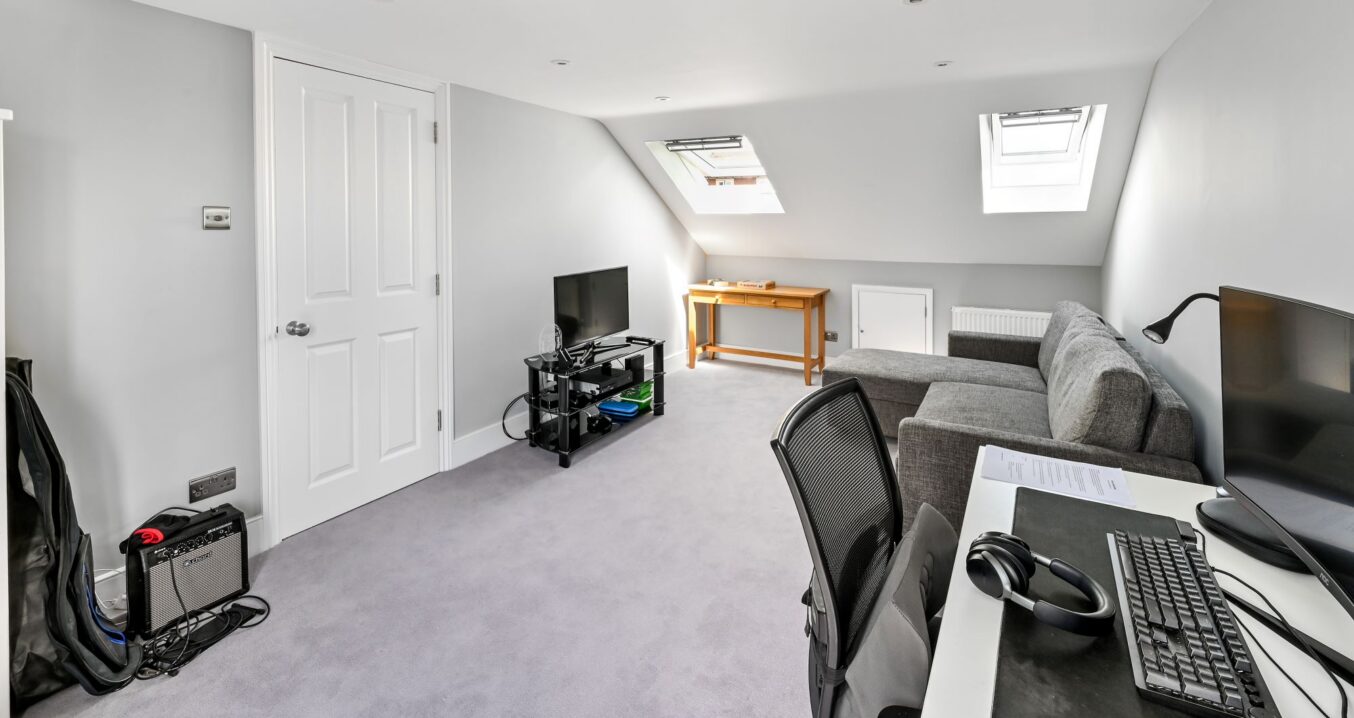 Loft room with a desk, computer, grey sofa and two rooflights.