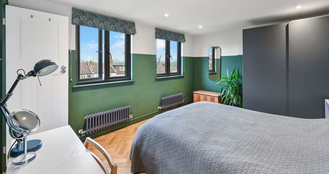 Loft main bedroom with green walls, black framed windows and herringbone flooring.