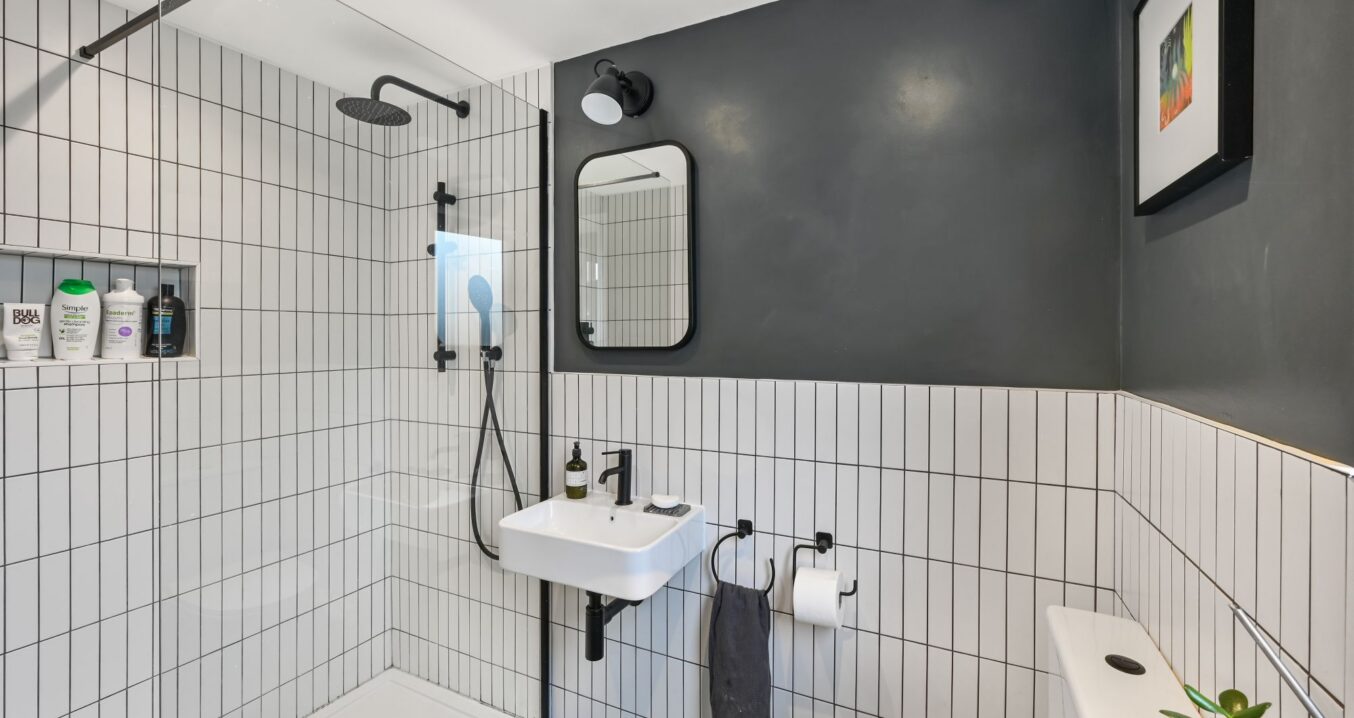 Loft shower room with white tiled walls, dark painted walls and black fittings.
