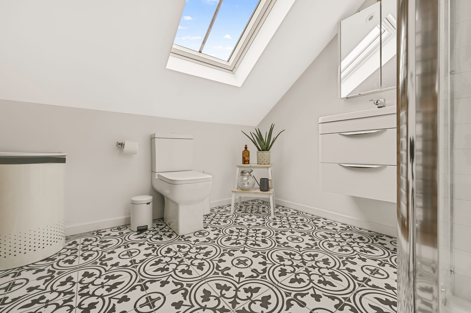 Compact loft shower room with patterned floor tiles, rooflight and sloping ceiling in Palmers Green N13.