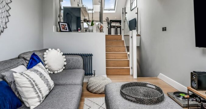 Modern loft lounge with sofa, television and steps up to a kitchen area, shown for the Palmers Green N13 Our Work page.