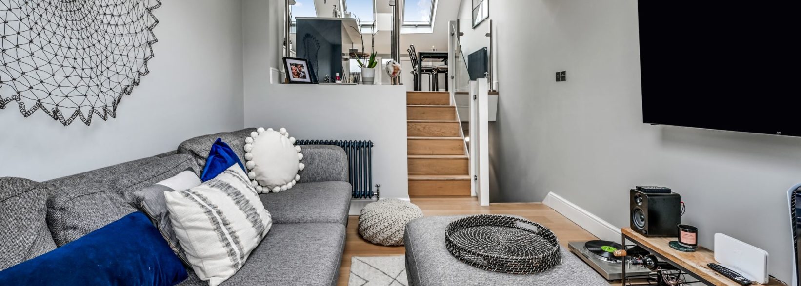 Modern loft lounge with sofa, television and steps up to a kitchen area, shown for the Palmers Green N13 Our Work page.