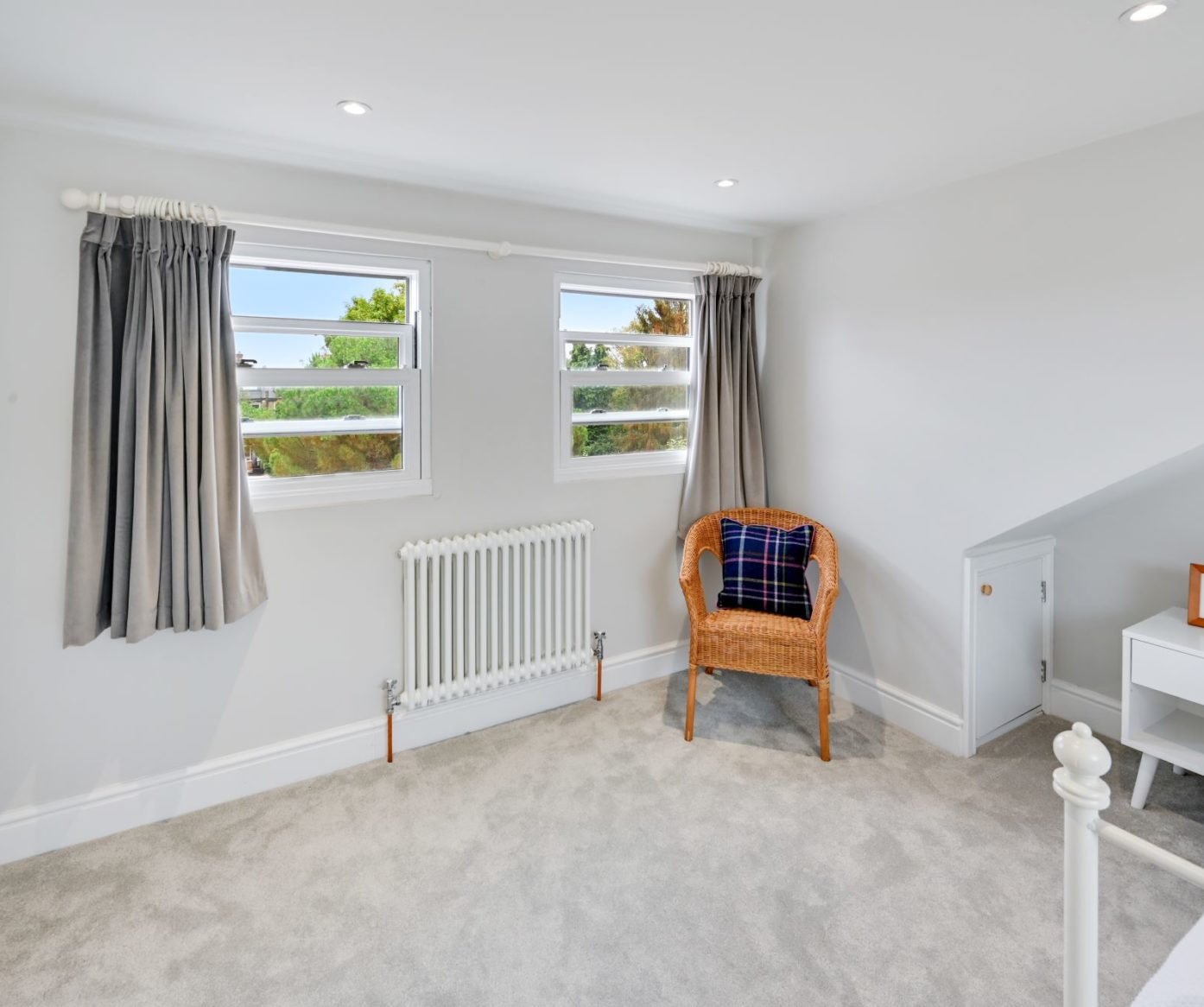 Bright loft bedroom with twin windows, grey carpet, low storage cupboard and neutral walls, supporting SE20 loft bedroom ideas.