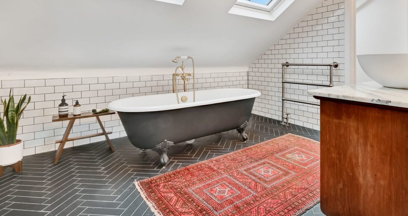 Loft bathroom with freestanding bath, rooflights, tiled walls and patterned rug, supporting Crystal Palace loft bathroom ideas.