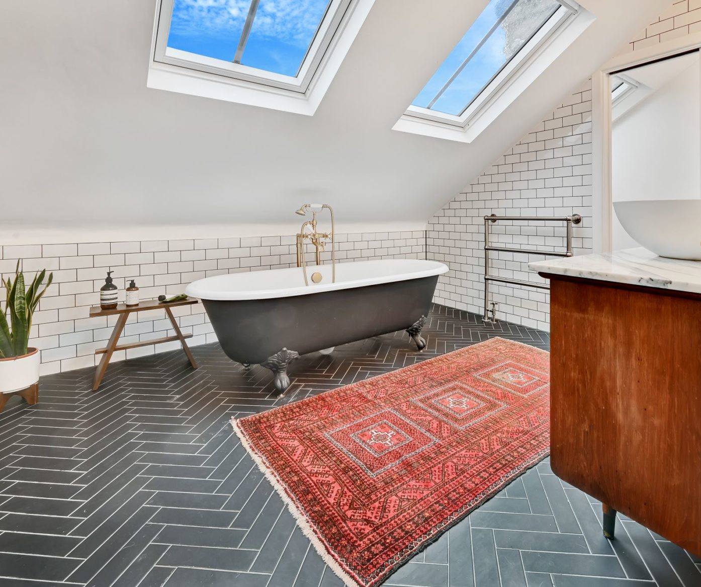 Loft bathroom with freestanding bath, rooflights, tiled walls and patterned rug, supporting Crystal Palace loft bathroom ideas.