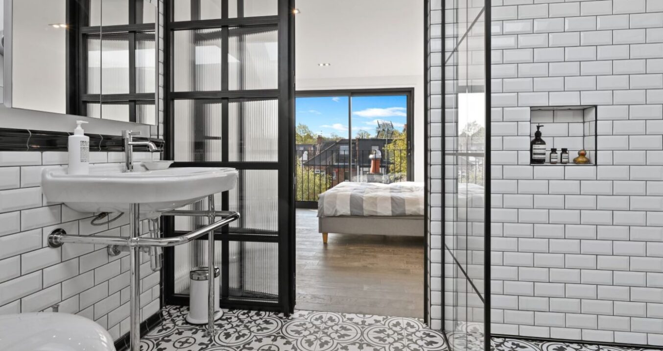 Loft shower room with white wall tiles, patterned floor, black-framed glazing and view through to a bedroom, supporting Crystal Palace loft ideas.