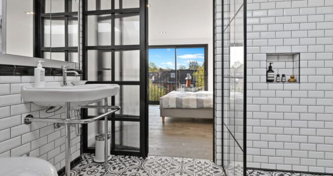 Loft shower room with white wall tiles, patterned floor, black-framed glazing and view through to a bedroom, supporting Crystal Palace loft ideas.