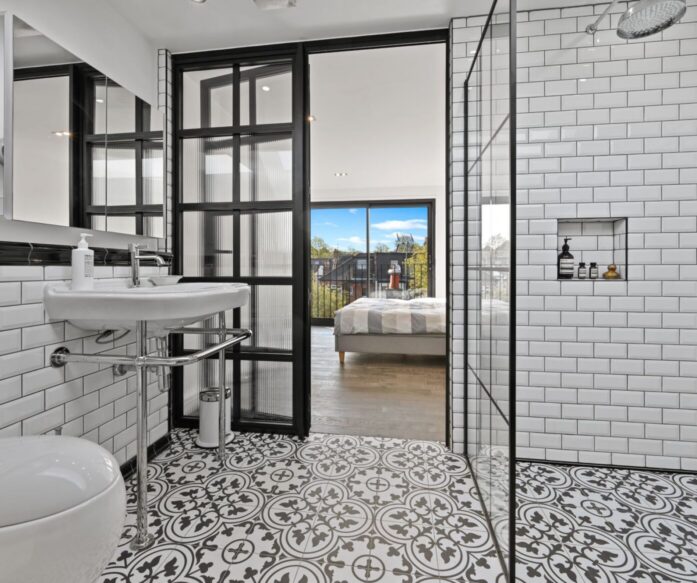 Loft shower room with white wall tiles, patterned floor, black-framed glazing and view through to a bedroom, supporting Crystal Palace loft ideas.