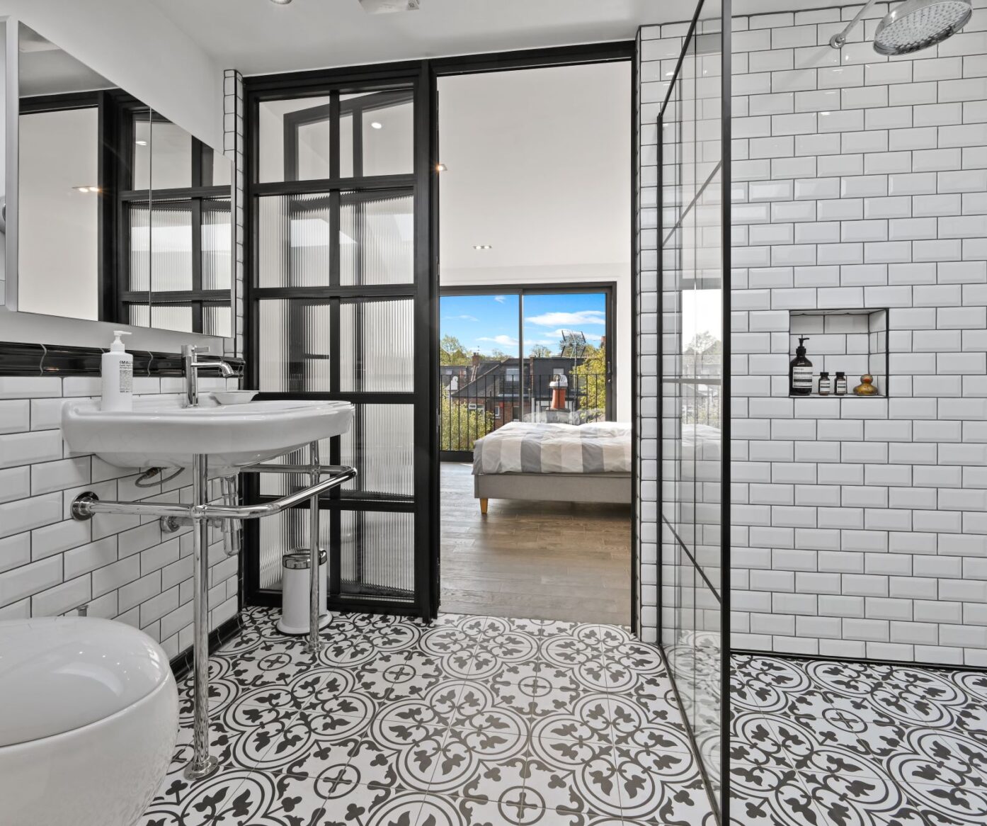 Loft shower room with white wall tiles, patterned floor, black-framed glazing and view through to a bedroom, supporting Crystal Palace loft ideas.