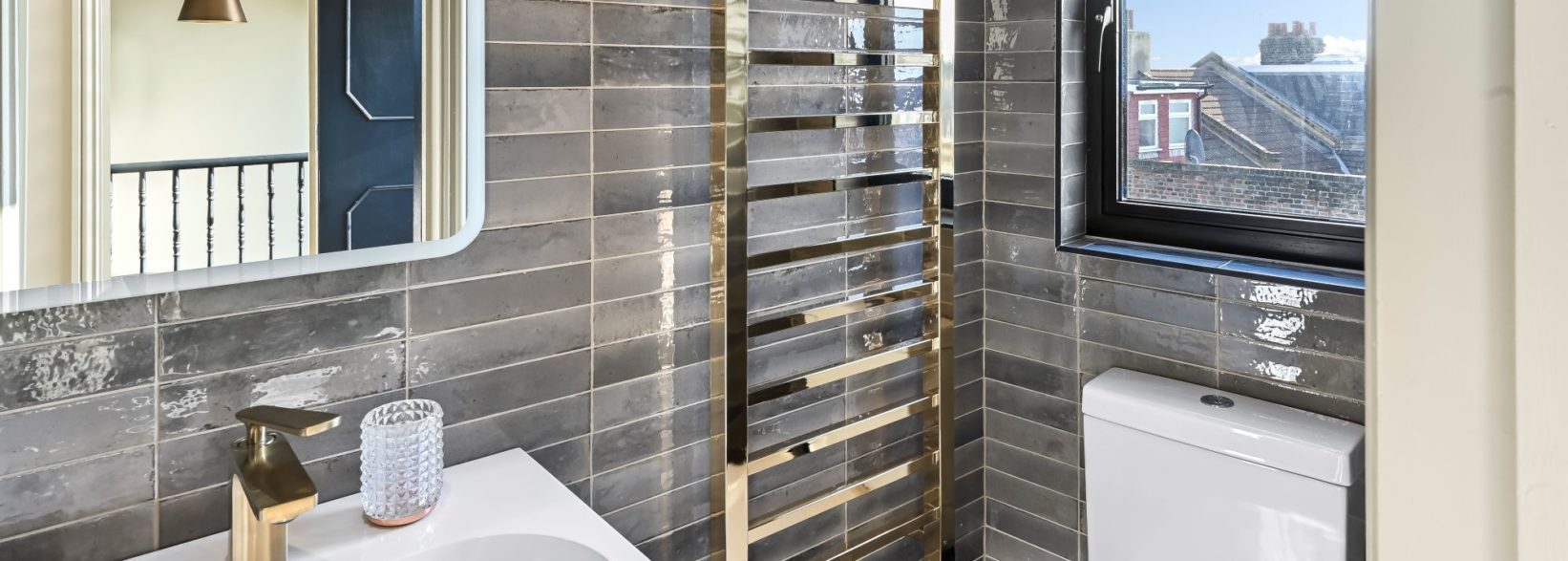 Grey tiled loft bathroom with basin, heated towel rail, modern fittings and window, supporting Crystal Palace loft conversion content.