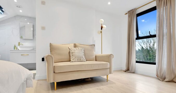 Large loft bedroom with sofa, wide window, pale flooring and en-suite area, supporting Crystal Palace main bedroom loft ideas.