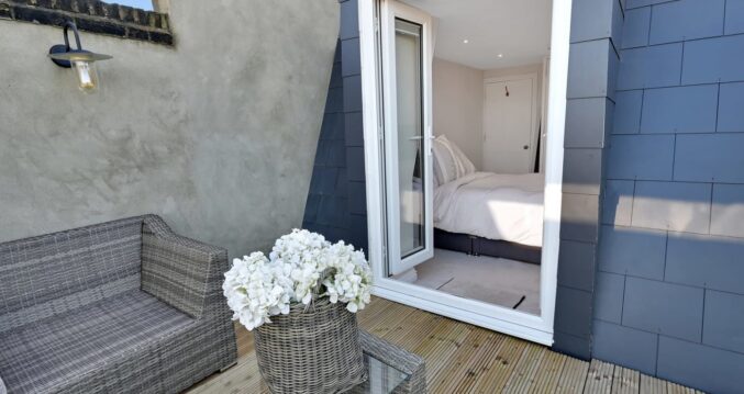 Mansard loft terrace with decked outdoor space, grey cladding and open bedroom doors, supporting Crystal Palace loft conversion ideas.