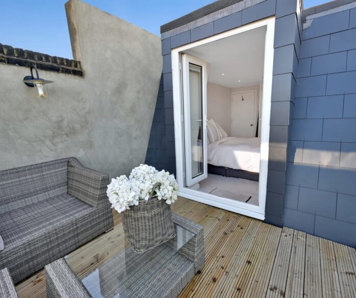 Mansard loft terrace with decked outdoor space, grey cladding and open bedroom doors, supporting Crystal Palace loft conversion ideas.
