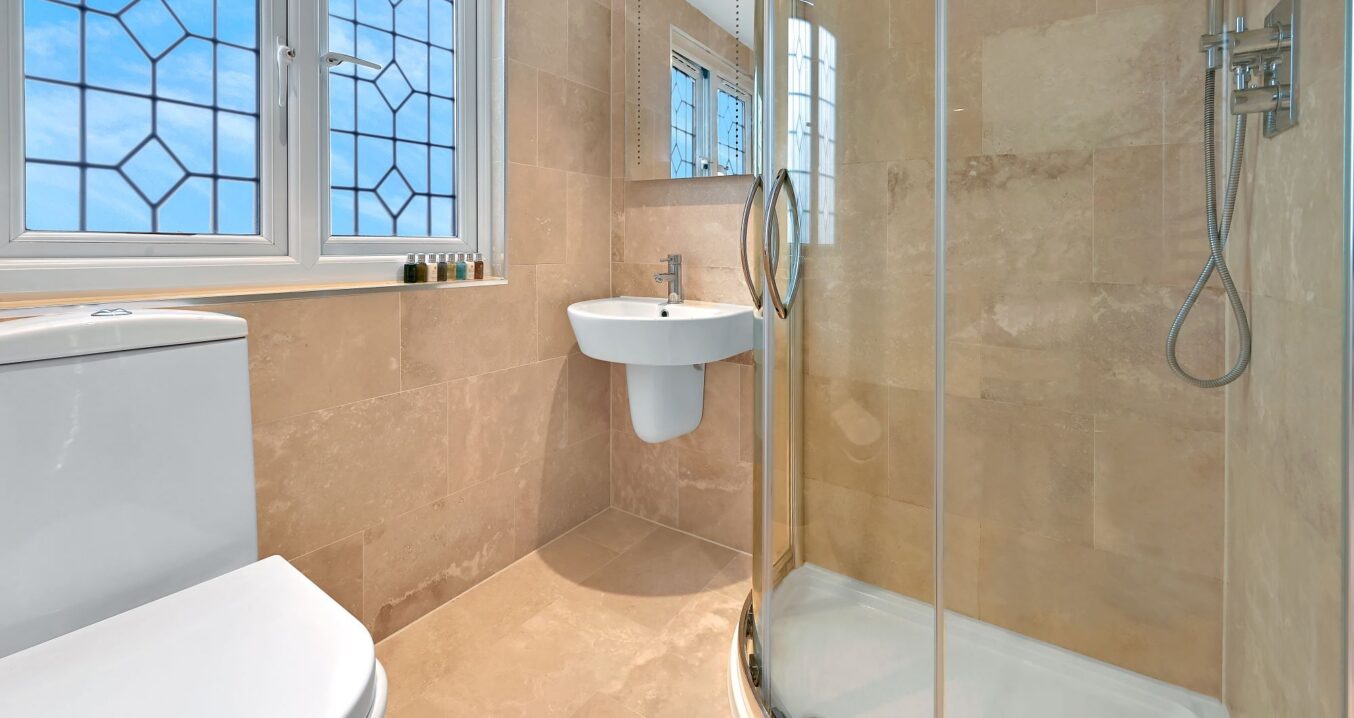 Tiled loft shower room with glass shower enclosure, basin and window in an Edgware HA8 loft conversion.