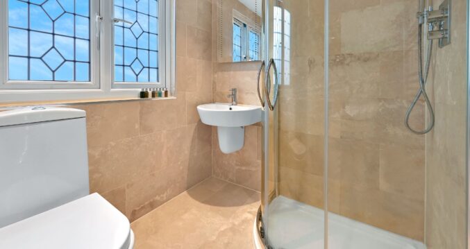 Tiled loft shower room with glass shower enclosure, basin and window in an Edgware HA8 loft conversion.