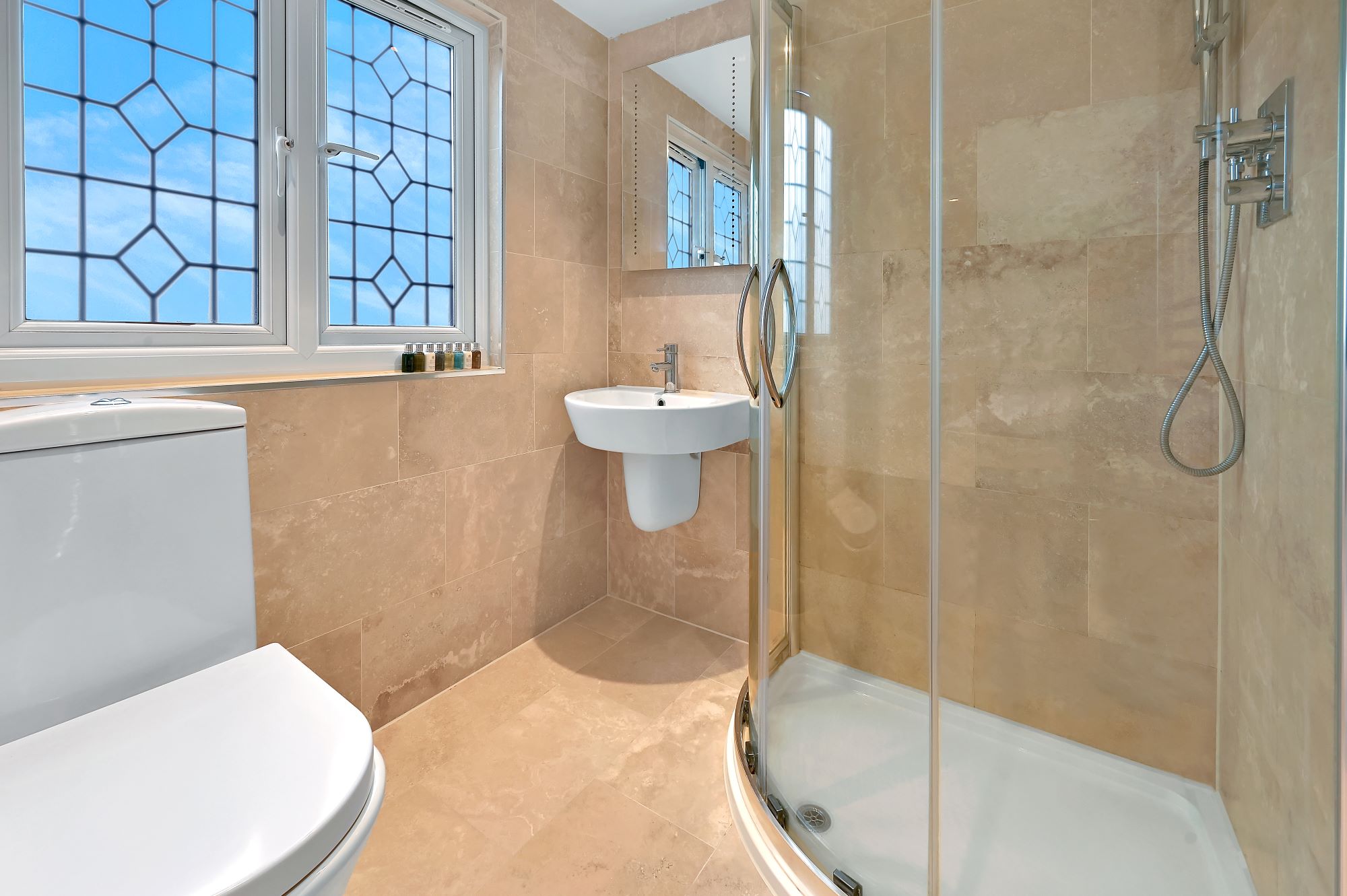 Tiled loft shower room with glass shower enclosure, basin and window in an Edgware HA8 loft conversion.