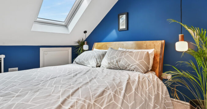 Loft bedroom with blue feature wall, rooflight, timber flooring and eaves storage for the Absolute Lofts Wood Green N22 loft conversion page.