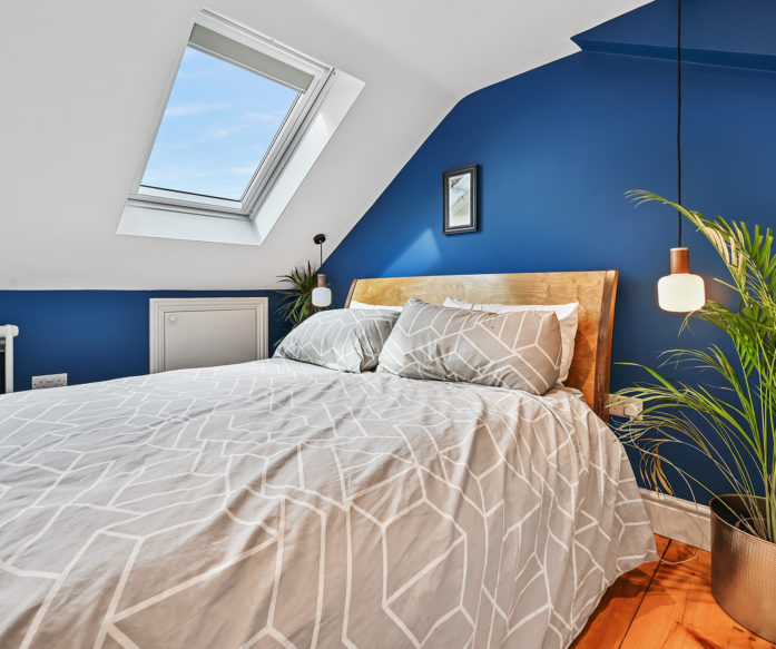 Loft bedroom with blue feature wall, rooflight, timber flooring and eaves storage for the Absolute Lofts Wood Green N22 loft conversion page.