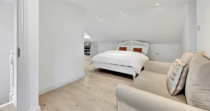 Bright loft bedroom with pale timber flooring, eaves storage, recessed lighting and sitting area for the Absolute Lofts Wood Green N22 page.