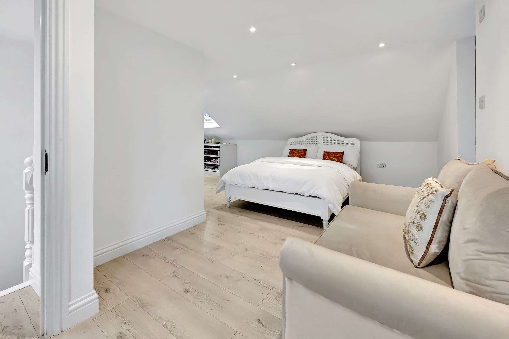 Bright loft bedroom with pale timber flooring, eaves storage, recessed lighting and sitting area for the Absolute Lofts Wood Green N22 page.