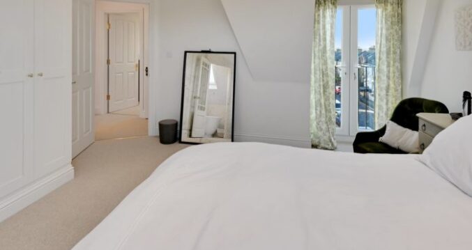 Dormer loft bedroom with fitted wardrobes, French doors and a glass balustrade in a Winchmore Hill N21 conversion