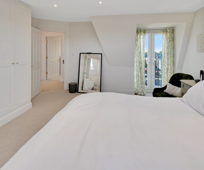 Dormer loft bedroom with fitted wardrobes, French doors and a glass balustrade in a Winchmore Hill N21 conversion