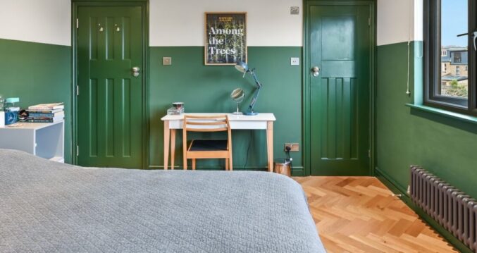 Green loft bedroom with herringbone timber flooring, fitted desk, dark doors and rear window for the Absolute Lofts Wood Green N22 page.
