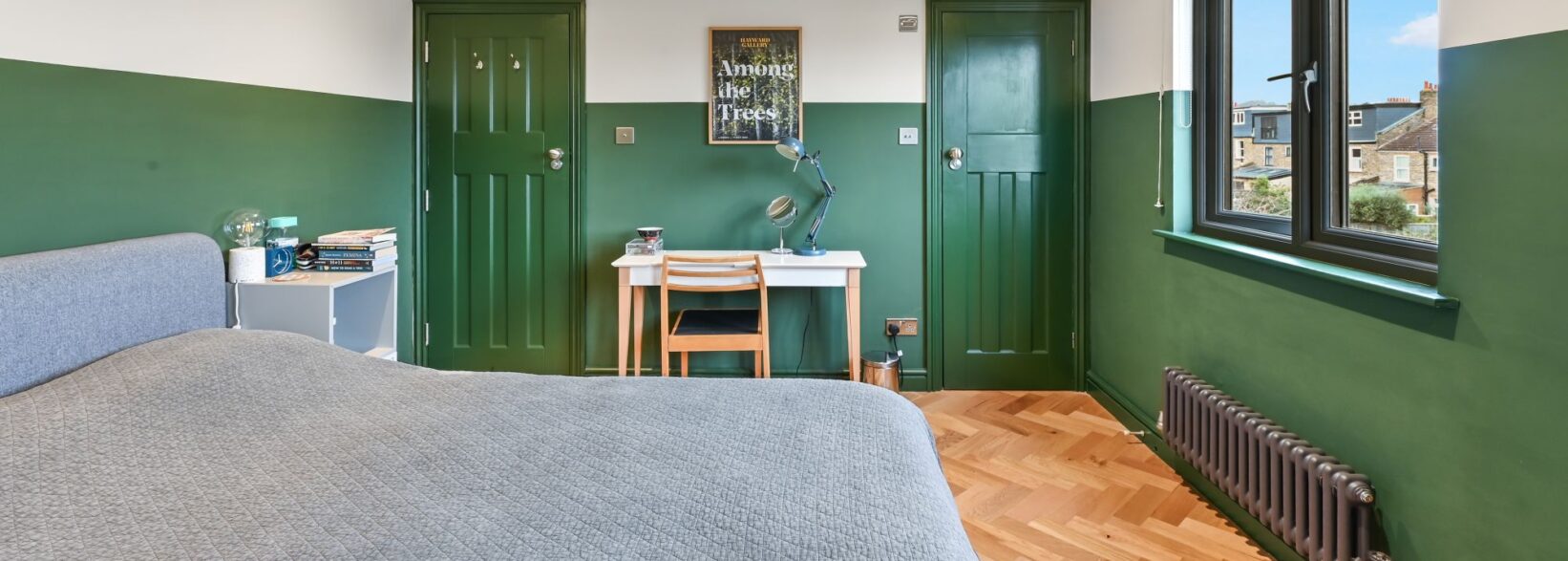 Green loft bedroom with herringbone timber flooring, fitted desk, dark doors and rear window for the Absolute Lofts Wood Green N22 page.