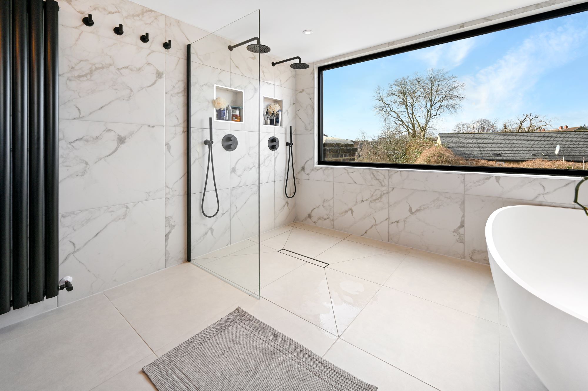 Luxury loft bathroom with walk in double shower, marble effect tiling, freestanding bath and wide picture window for the Wood Green N22 page.