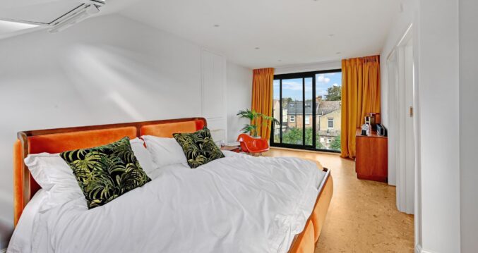 Spacious loft bedroom with full height black framed glazing, timber flooring and contemporary finishes for the Wood Green N22 loft conversion page.