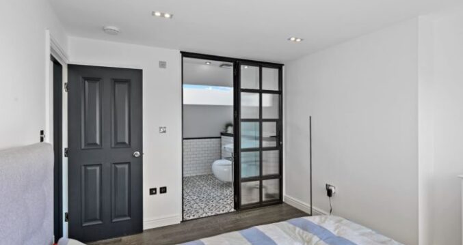 Loft bedroom with dark doors and a black framed glazed ensuite entrance for the Absolute Lofts Wood Green N22 loft conversion page.