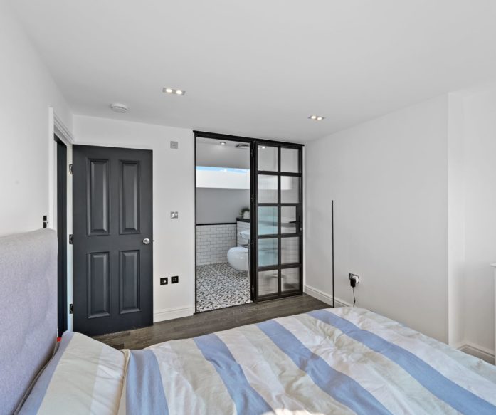 Loft bedroom with dark doors and a black framed glazed ensuite entrance for the Absolute Lofts Wood Green N22 loft conversion page.