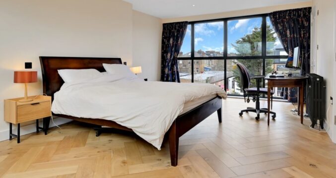 Large loft bedroom with herringbone timber flooring, fitted storage and full width rear glazing for the Absolute Lofts Wood Green N22 page.
