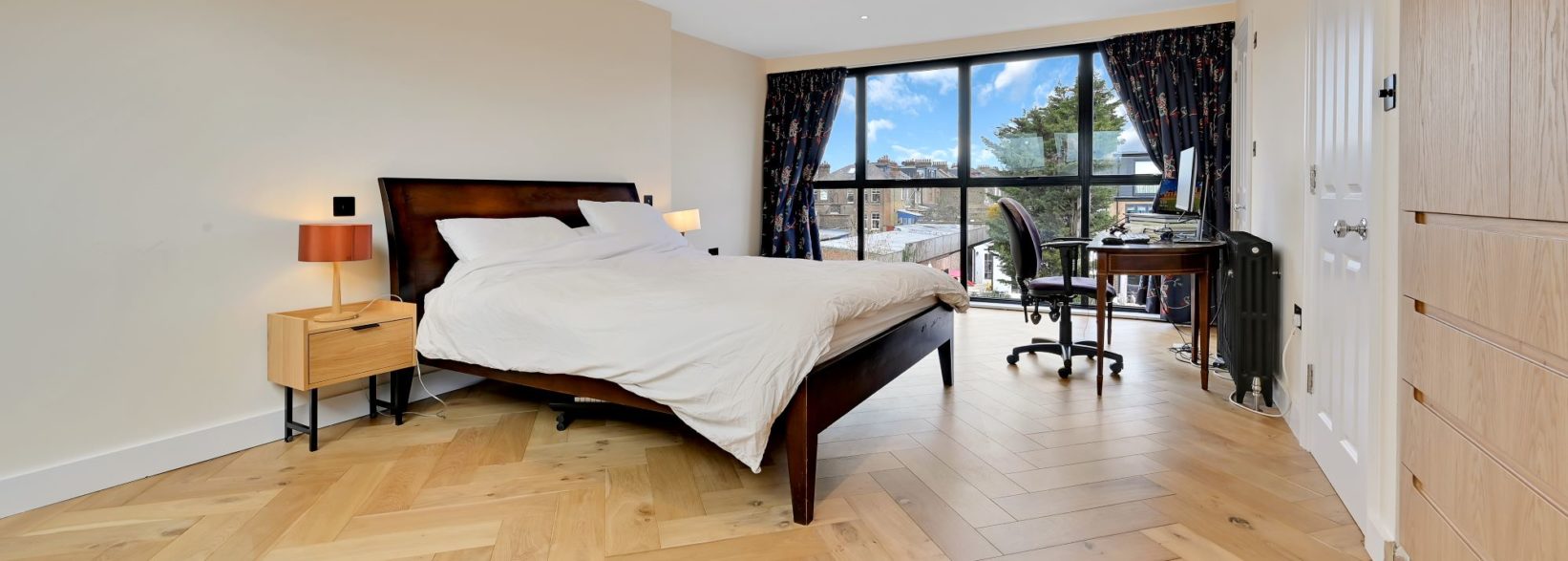 Large loft bedroom with herringbone timber flooring, fitted storage and full width rear glazing for the Absolute Lofts Wood Green N22 page.