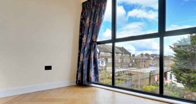 Finished loft room with full width black framed rear glazing, timber flooring and wide rooftop views for the Wood Green N22 loft conversion page.