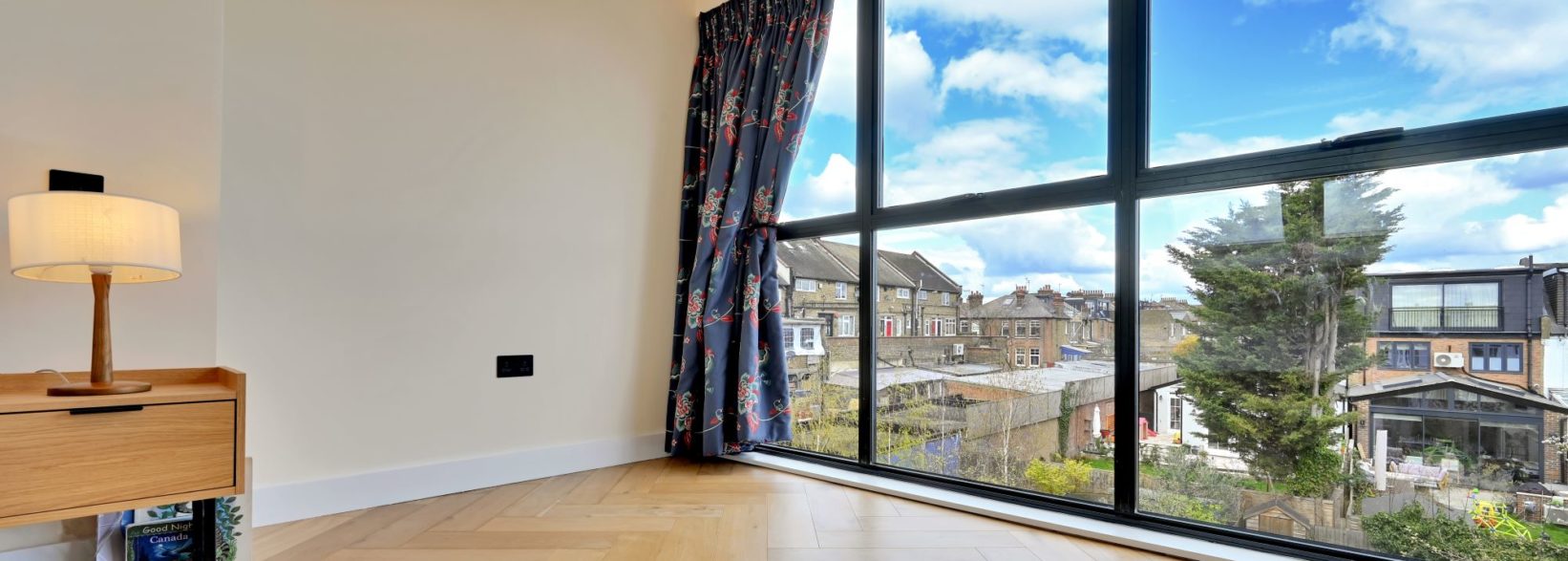 Finished loft room with full width black framed rear glazing, timber flooring and wide rooftop views for the Wood Green N22 loft conversion page.
