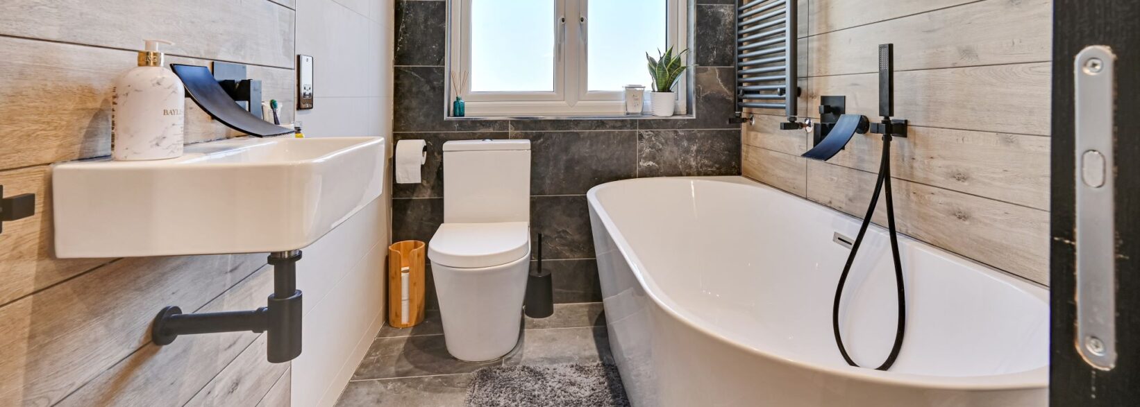 Modern loft bathroom with a freestanding bath, black fittings and timber effect wall tiles in Winchmore Hill N21